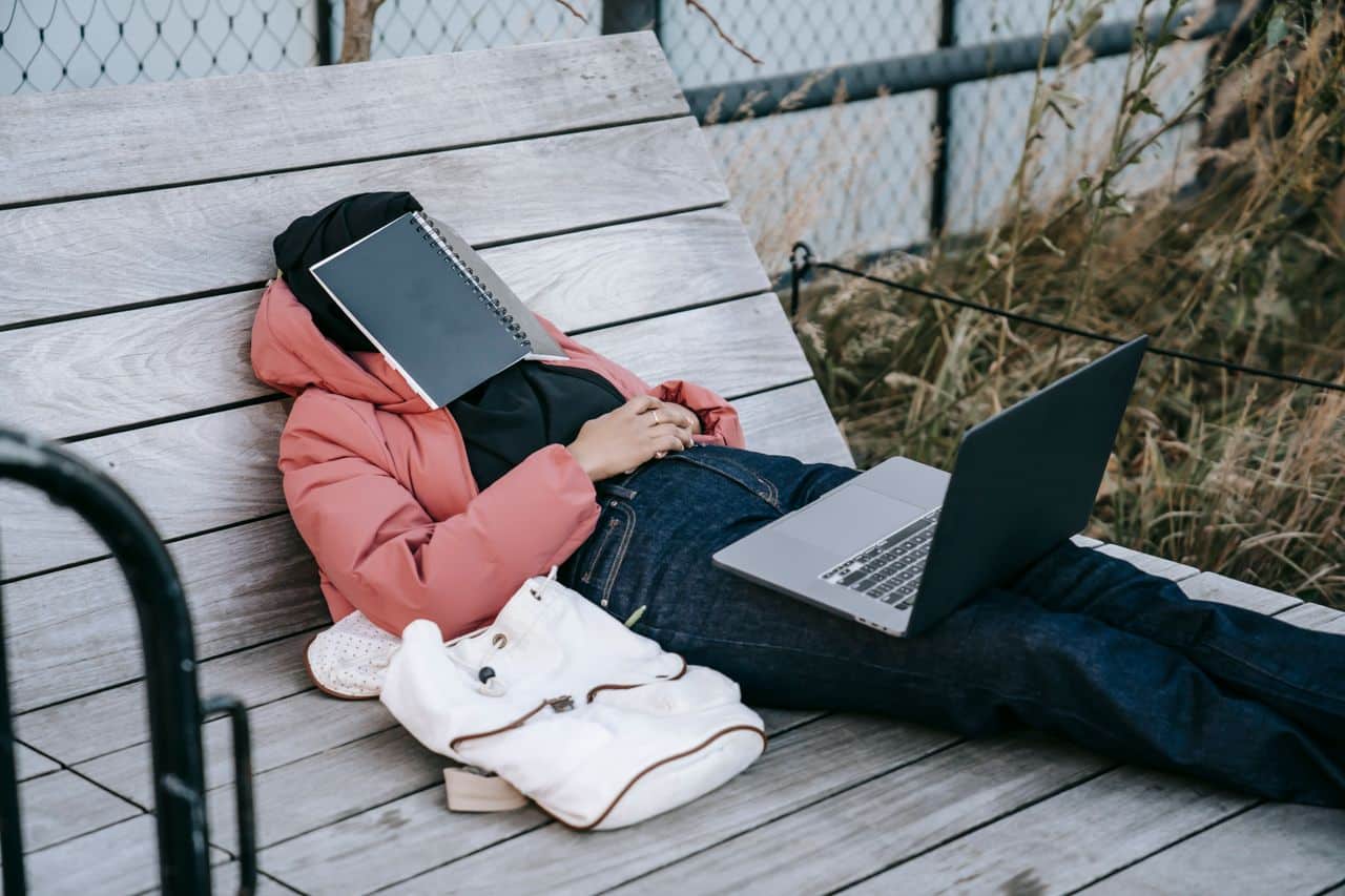 A visual representation of a person laying on a chair with a book covering their face while sleeping, and a computer on their lap.